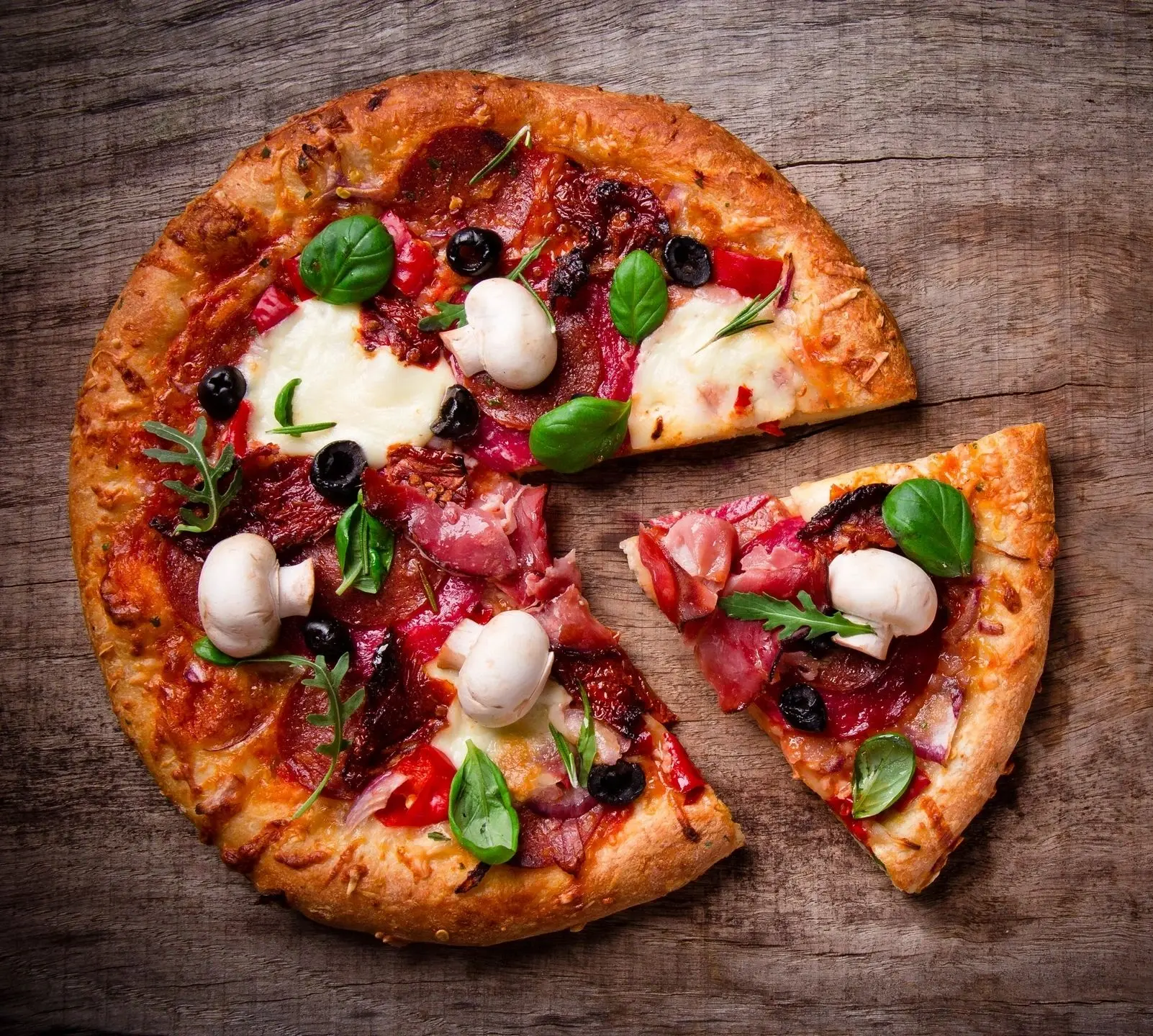 A pizza cut in half on top of a wooden table.