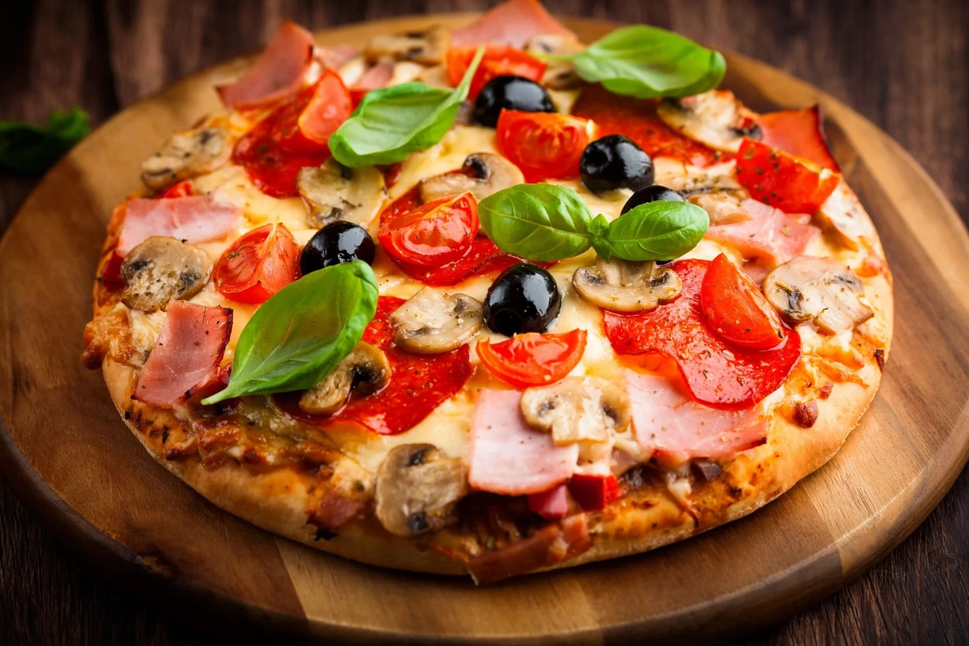 A pizza with tomatoes, olives and ham on top.